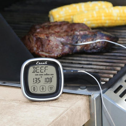 the touch screen thermometer and timer displayed sitting beside an open grill with food