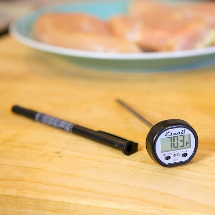 the digital pocket thermometer displayed on a wood surface with plate of food in the background