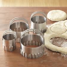 biscuit cutters on counter with rolled dough with biscuits cut out of it.