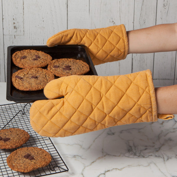 hands wearing mitts holding pan of cookies.