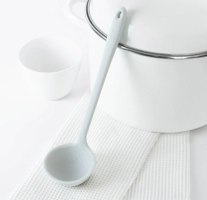ladle laying on a white dishtowel and leaning against a pot on a white countertop.