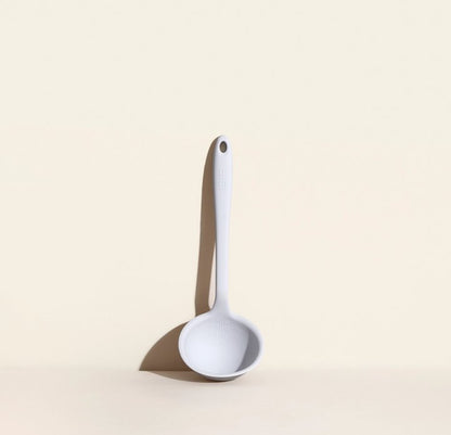 ladle leaning against a cream colored background.