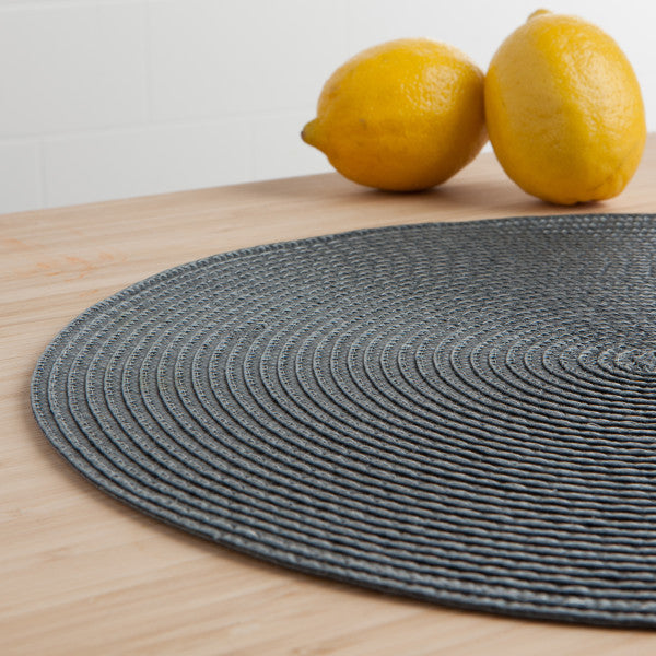angled view of the charcoal disko placemat displayed on a light wooden surface next to two limes