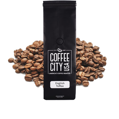 a black coffee bag filled with english toffee coffee with a pile of coffee beans behind it on a white background
