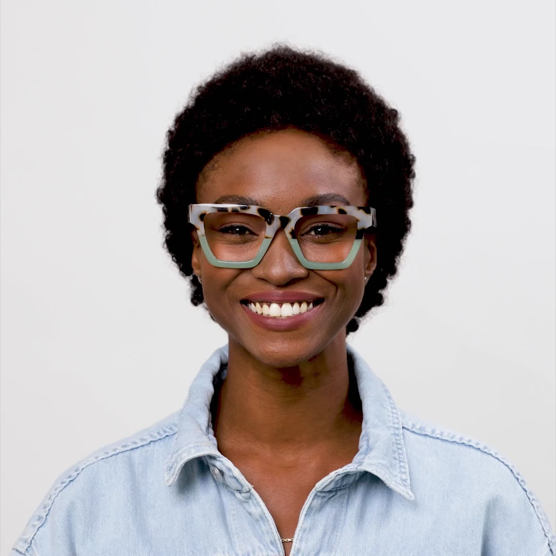 video of a woman modeling the chai tortoise and green take a bow glasses and turning her head to show both sides against a cream background