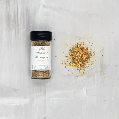 jar of all purpose seasoning laying down next to a scatter pile of seasoning on a white surface