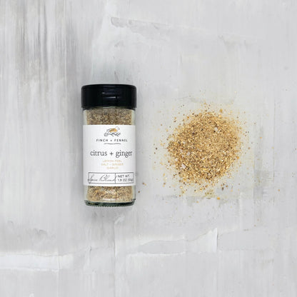 jar of citrus and ginger spice blend laying down next to a scatter pile of seasoning on a white surface