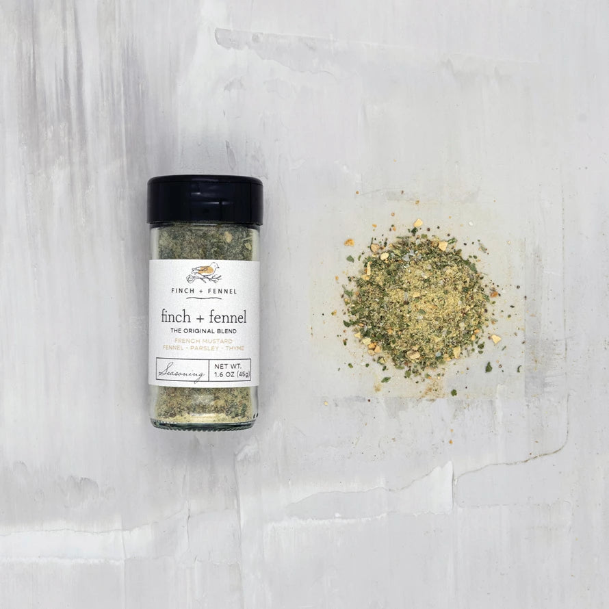 jar of finch and fennel blend laying down next to a scatter pile of seasoning on a white surface