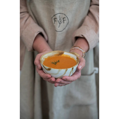 close up of a womans hand cupping a bowl of soup made with the basque seasoning blend