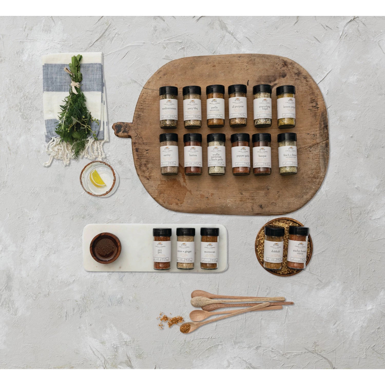 multiple jars of seasoning laying on a wooden board next to a striped towel, spice spoons, and plate of spice jars