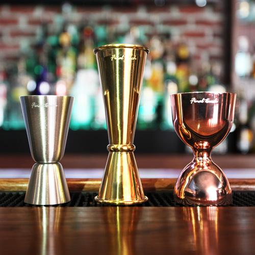 the mixed metal double jigger set displayed in a bar on a counter