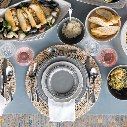 table display with dinnerware place setting, flatware, glasses, serving bowls with food on a gray tablecloth