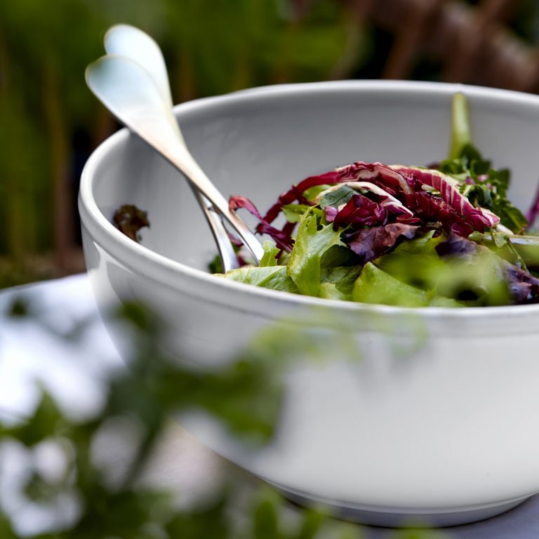 white serving bowl filled with greens and serving utensils.