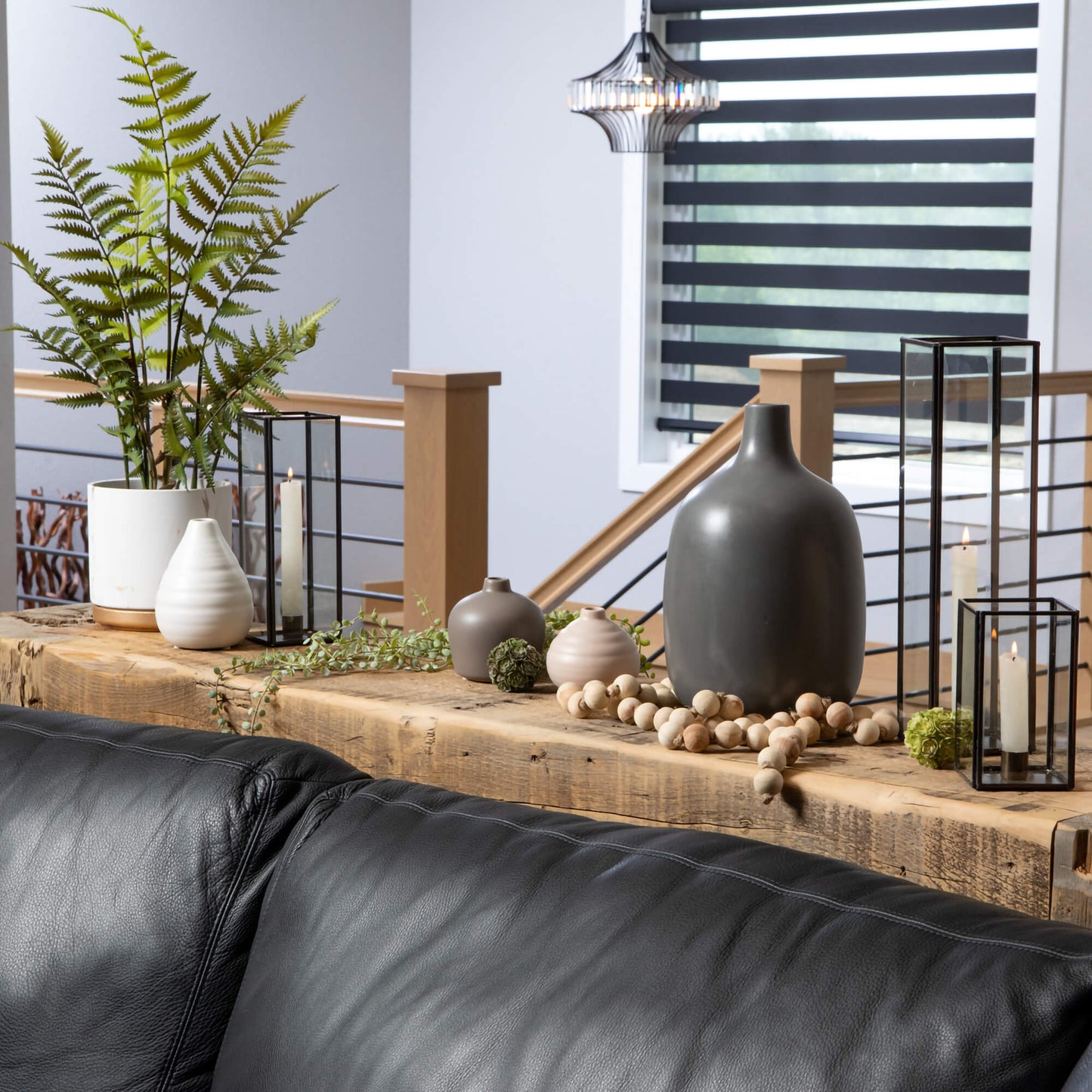 wood table behind a black couch, table has several white, black, and grey vase arranged on it and a bead garland draped along it.