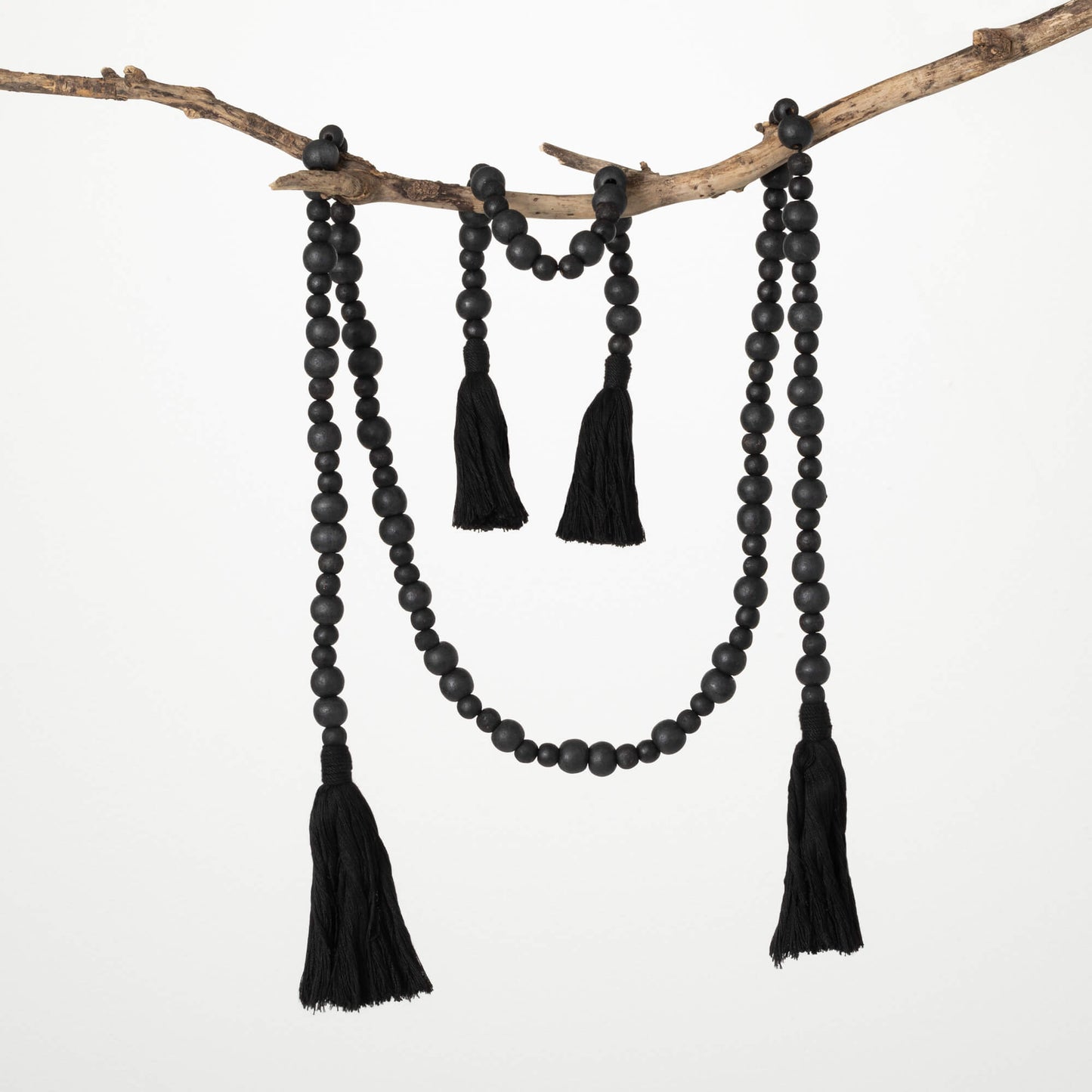 large and small black beaded garlands with tassels on each end draped over a branch.