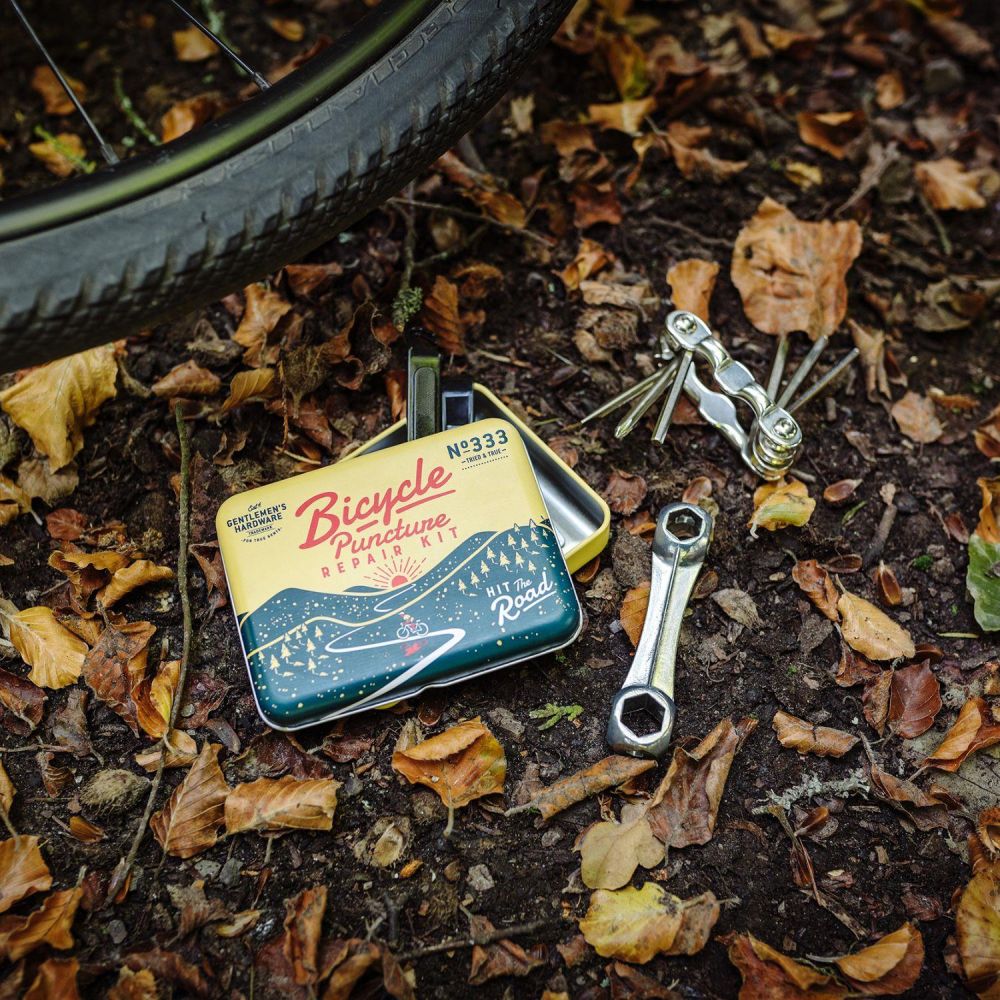 the open bicycle puncture repair kit displayed on a leaf covered ground with a bike tire in the background