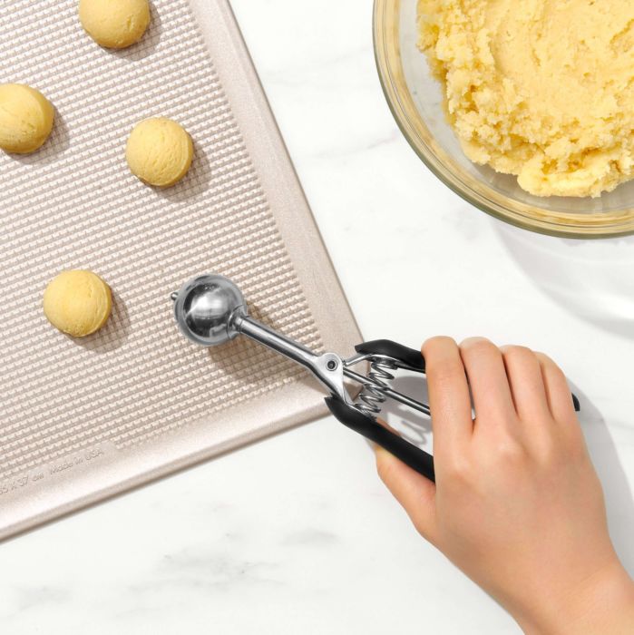 hand putting scoop of dough onto baking sheet.