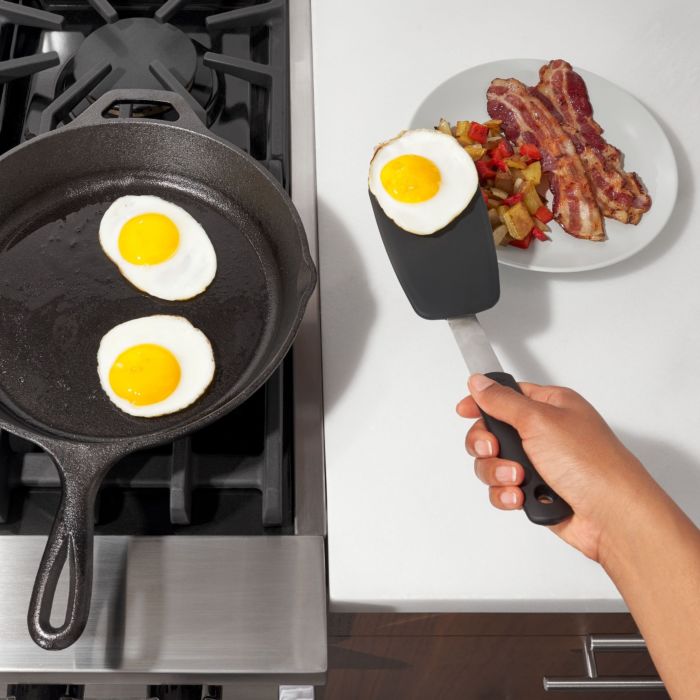 hand holding spatula moving fried egg from pan to plate.