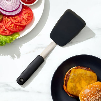 spatula set between plate with cheese burger on it and plate of lettuce, tomato, and onion.