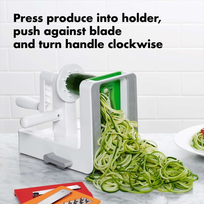 spiralizer on counter with cut zucchini and text "press produce into holder, push against blade and turn handle clockwise".