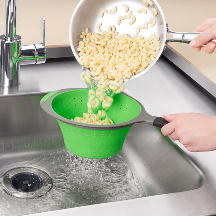 hands holding colander and pan of pasta being poured into it.