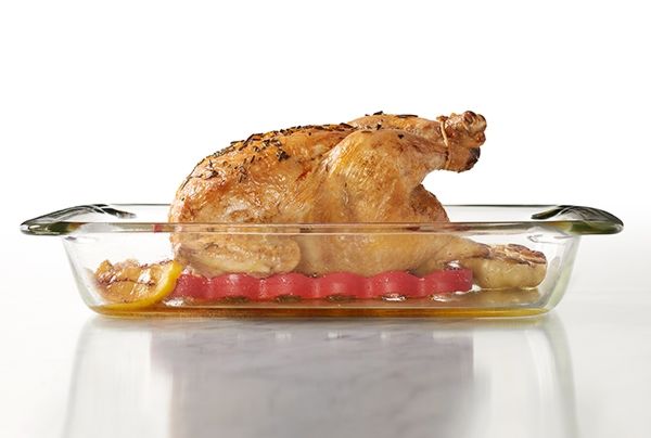 silicone roasting rack being used under a roasted bird in a glass rectangle baker against a white backgroud