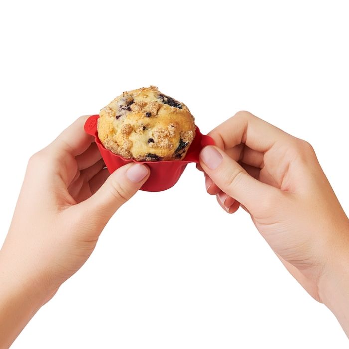 hand removing baking cup from muffin.
