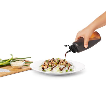 hand pouring soy sauce onto plate of rice with squeeze bottle, cutting board with chives and knife in background.