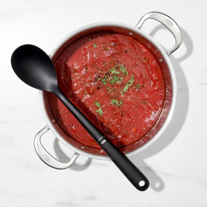 black spoon laying across pot of tomato sauce.