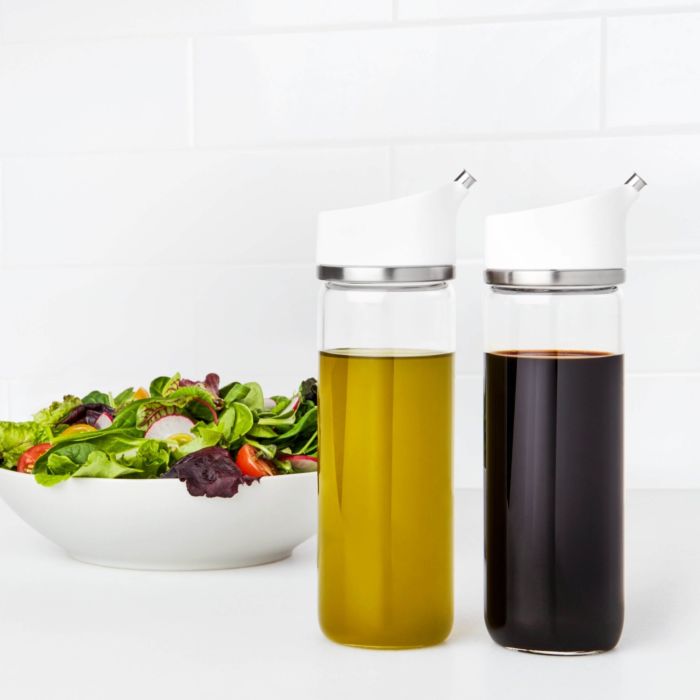  bottles filled with oil and vinegar with salad in background.