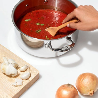 hand holding spoon sitrring red sauce in pot.