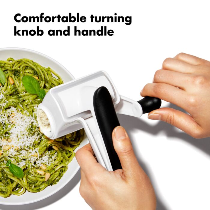 hands grating cheese over plate of pasta with text "comfortable turning knob and handle.