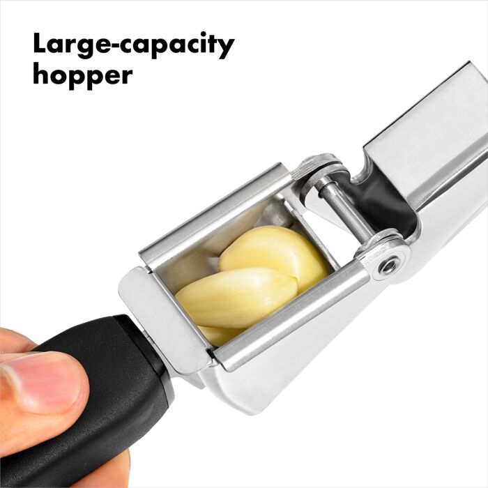 a persons hand holding the open garlic press showing the large capacity to hold garlic against a white background