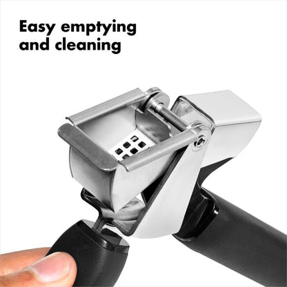 a persons hand holding the garlic press illustrating how easy it is to empty and clean it against a white background