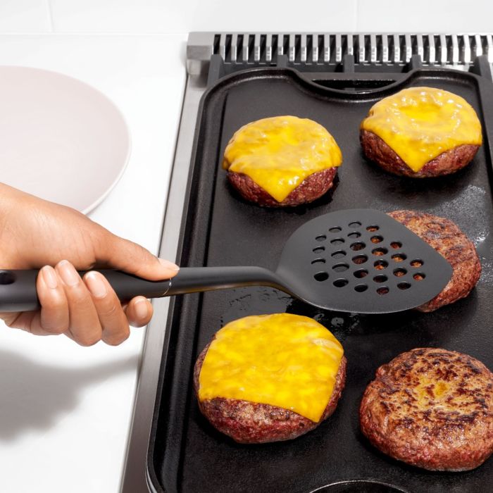 hand holding turner over burgers on grilling plate.