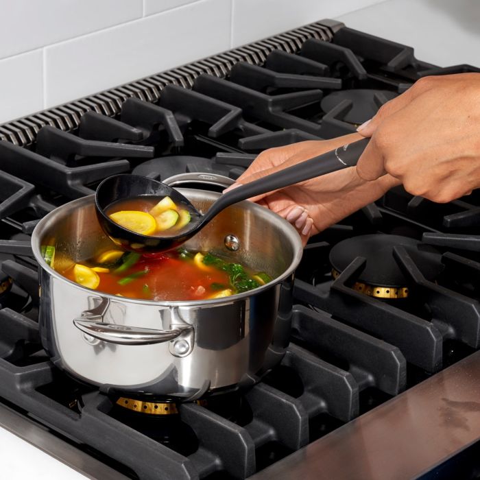 hands holding ladle and pot with soup in them.