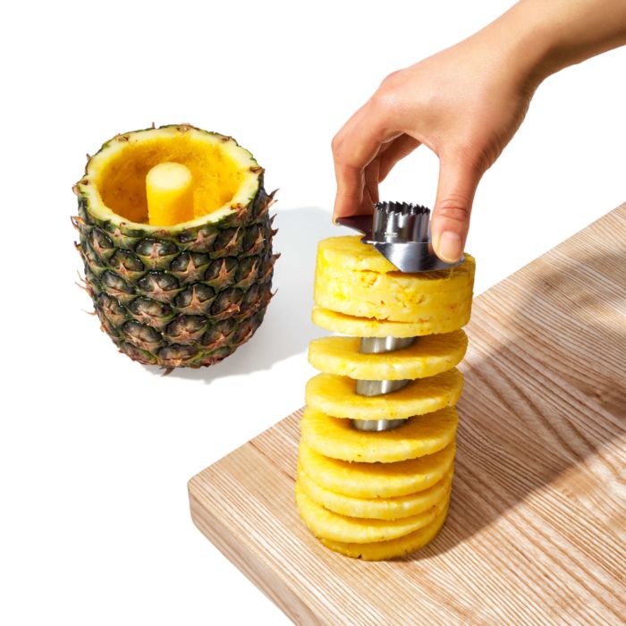 hand holding slicer with pineapple rings on it and hollowed out pineapple next to it.