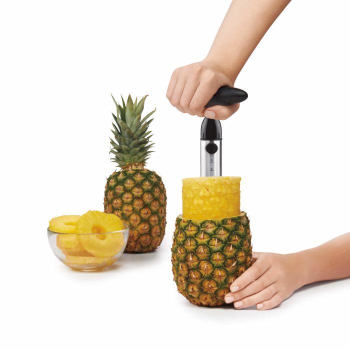 hands removing sliced pineapple from rind, whole pineapple and bowl of sliced pineapple in background.