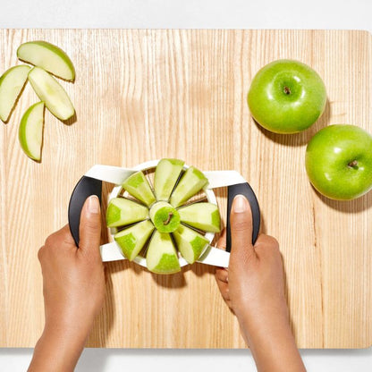 hands pressing slicer onto apple on wood board with green apples.