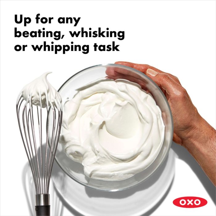 hand holding bowl of whipped cream and whisk with whipped cream on it.