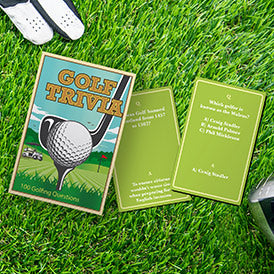 the golf trivia package and two trivia cards displayed next to a golf glove and club on the grass