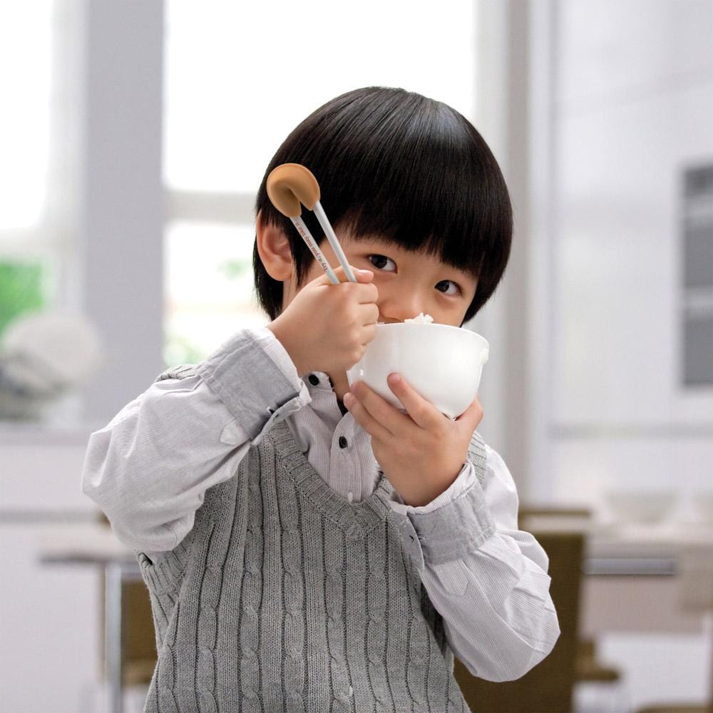 a young boy demonstrating how to use the good fortune chopstick while eating a bowl of rice