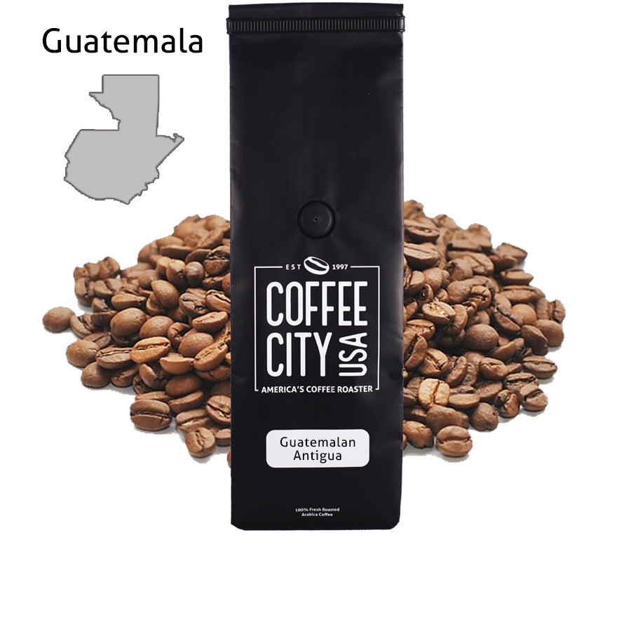 a black coffee bag filled with guatemalan antigua coffee with a pile of coffee beans behind it on a white background