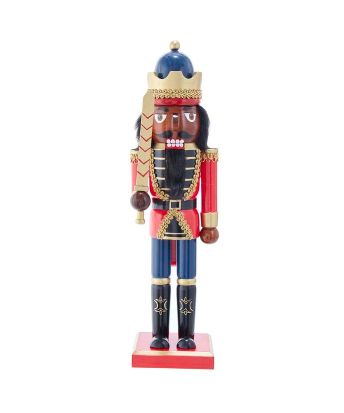 wooden nutcracker with dark skin tone wearing a red coat and blue pants all adorned with gold trim. he is wearing a crown and holding a gold sword.