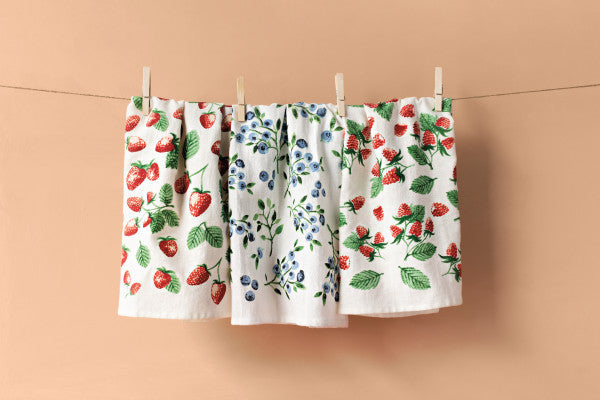 3 berry printed dishtowels clipped on a line with a peach colored background.