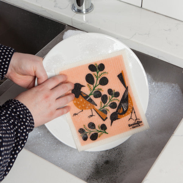hands using swedish dishcloth to wash dishes in kitchen sink.