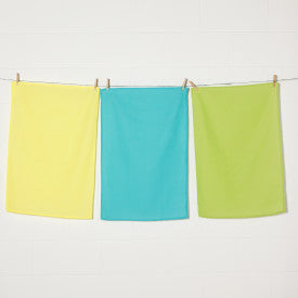 3 flour sack dishtowels hanging on line with clothespins: one each of yellow, teal, and lime green.