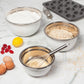 mixing bowls filled with batter, flour, and oats on countertop with eggs, whisk, and muffin pan.