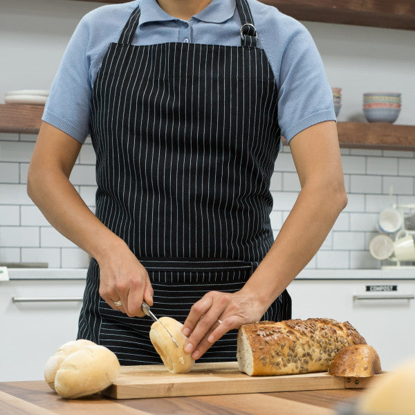 person wearing apron in kitchen while slicing bread.
