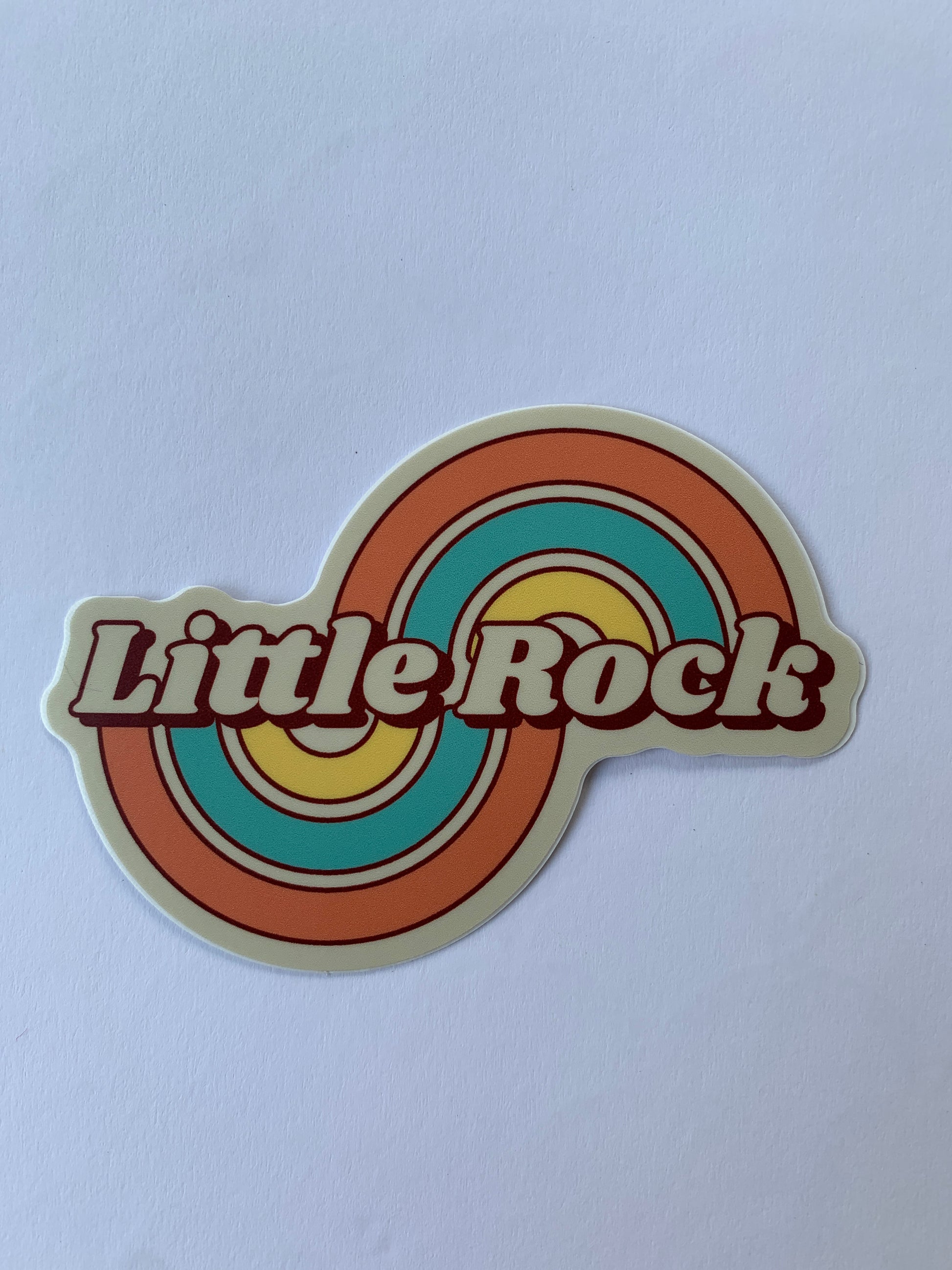 sticker on white background. sticker has graphic of swirling rainbow with "little rock across the center in retro type font.